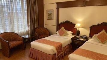 A hotel room with two beds, a chair, a small table, and a lamp.