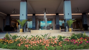 Fachada de hotel con una fuente central, grandes columnas y un jardín de flores.