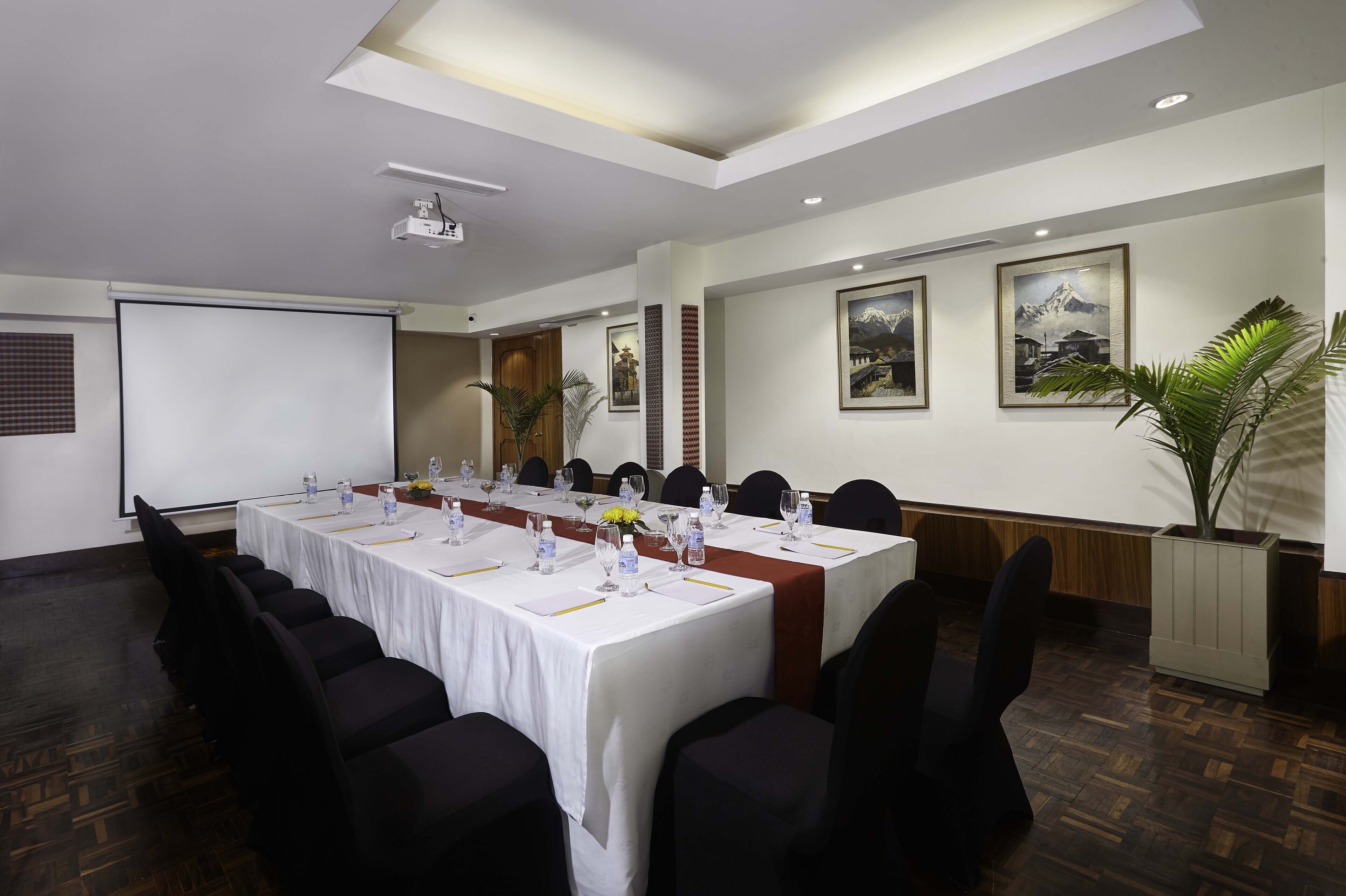 A conference room with a long table, chairs, a projector, and framed pictures on the walls.
