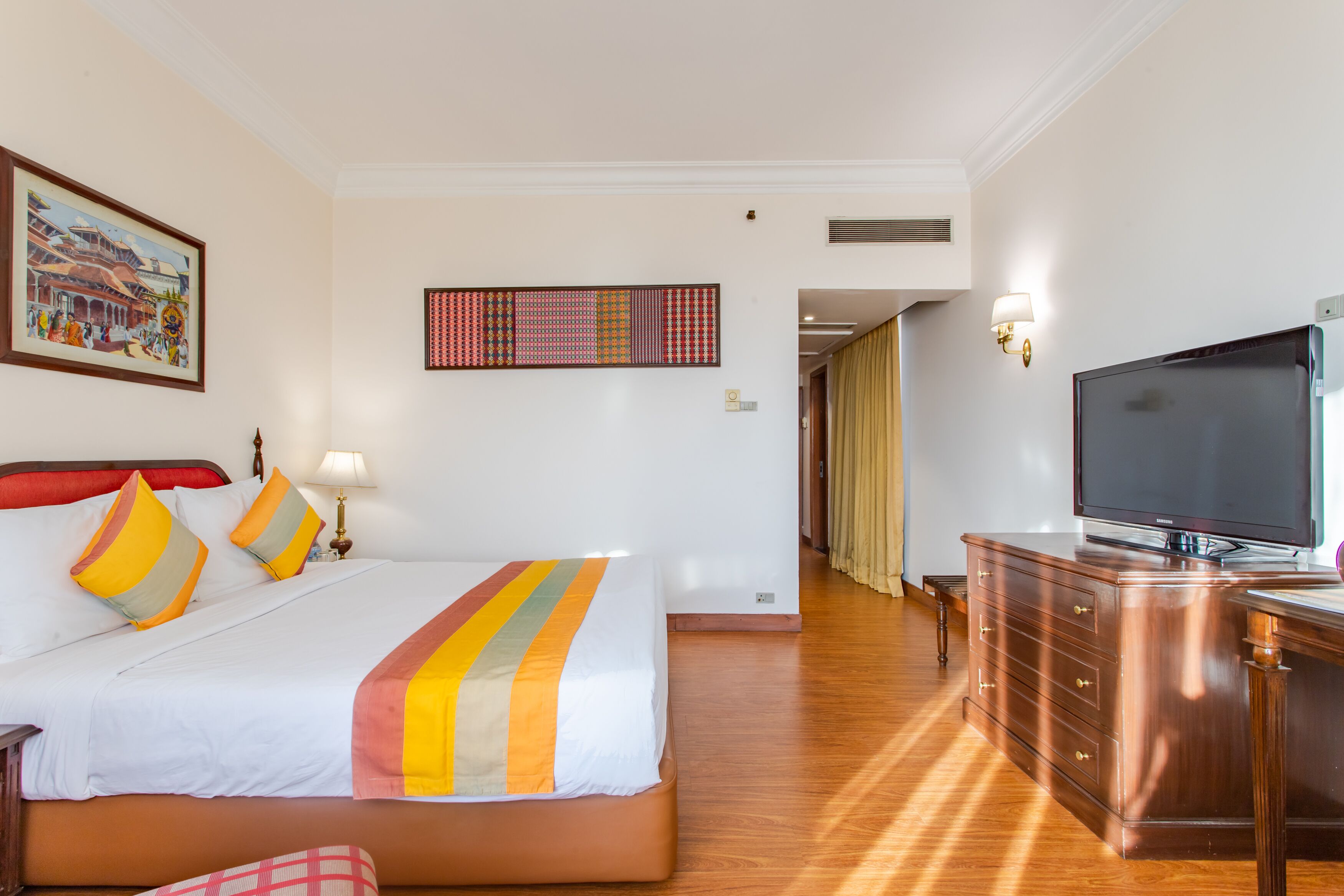 A hotel room with a large bed, a TV, a wooden dresser, and a painting on the wall.