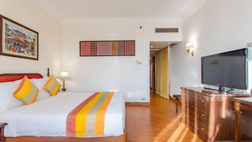 A hotel room with a large bed, a TV, a wooden dresser, and a painting on the wall.