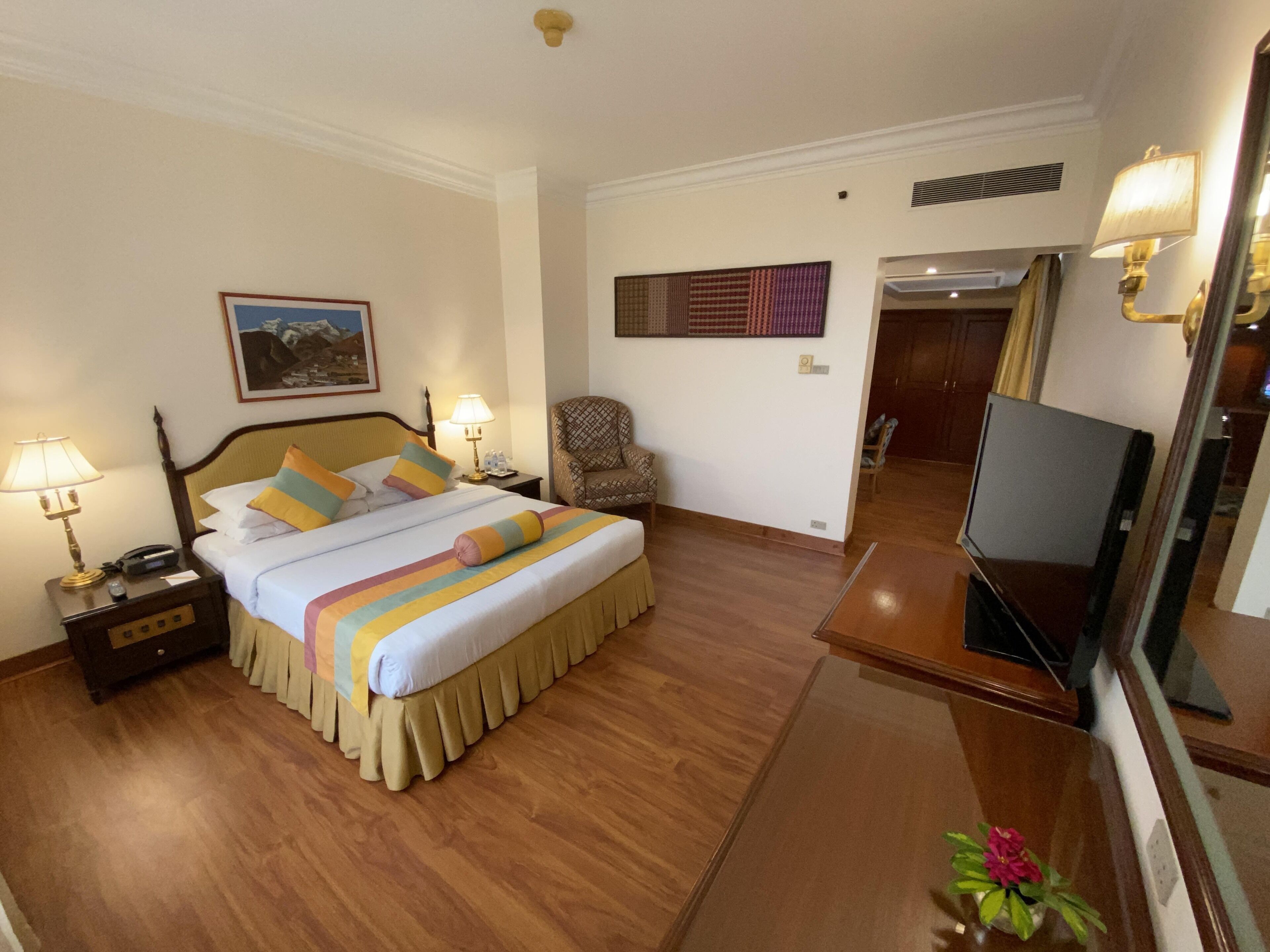 Una habitación de hotel con cama, lámparas de noche, una silla, televisor y espejo.