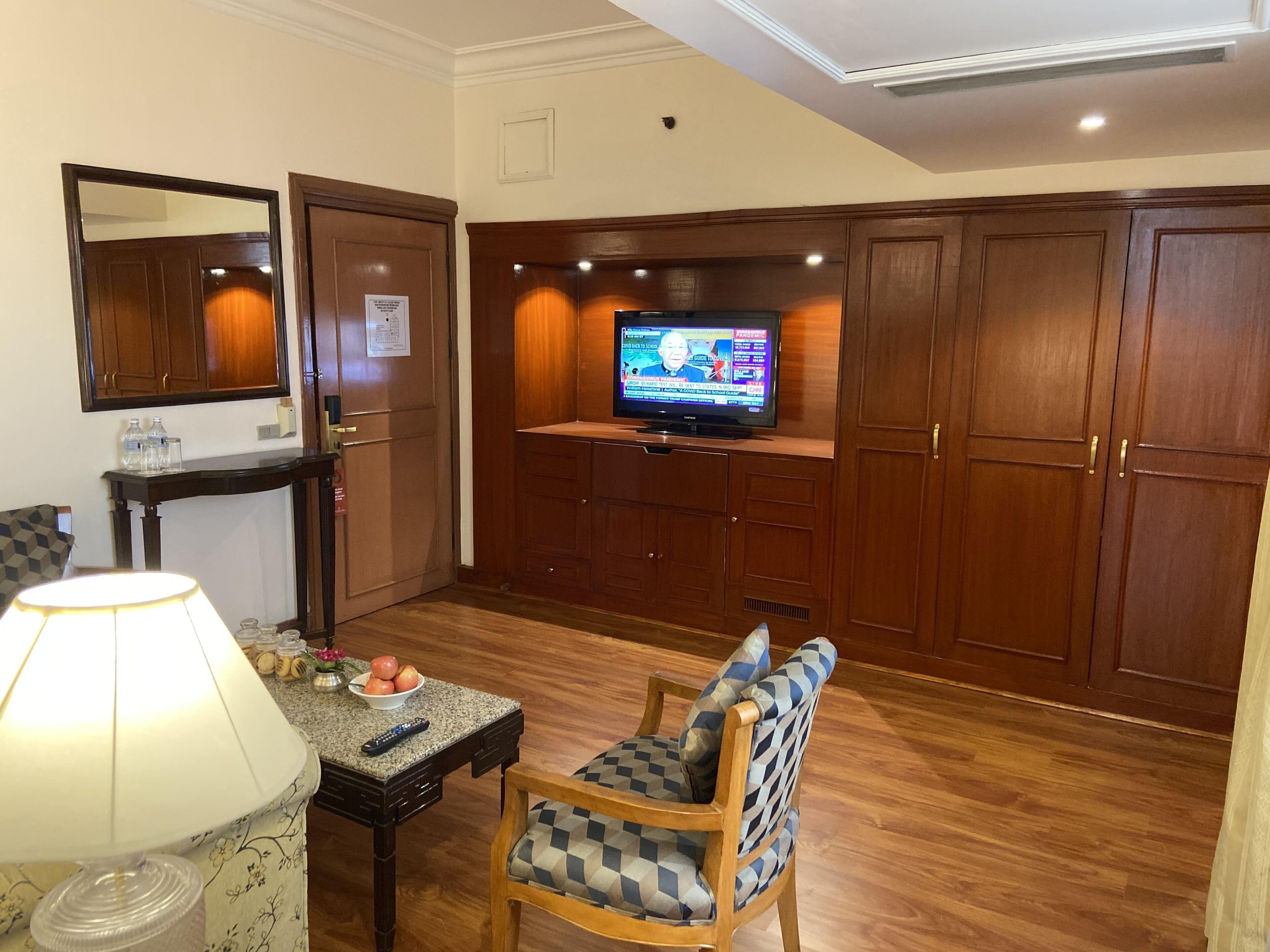 A living room with a television, wooden cabinets, a table with a lamp, and a chair.