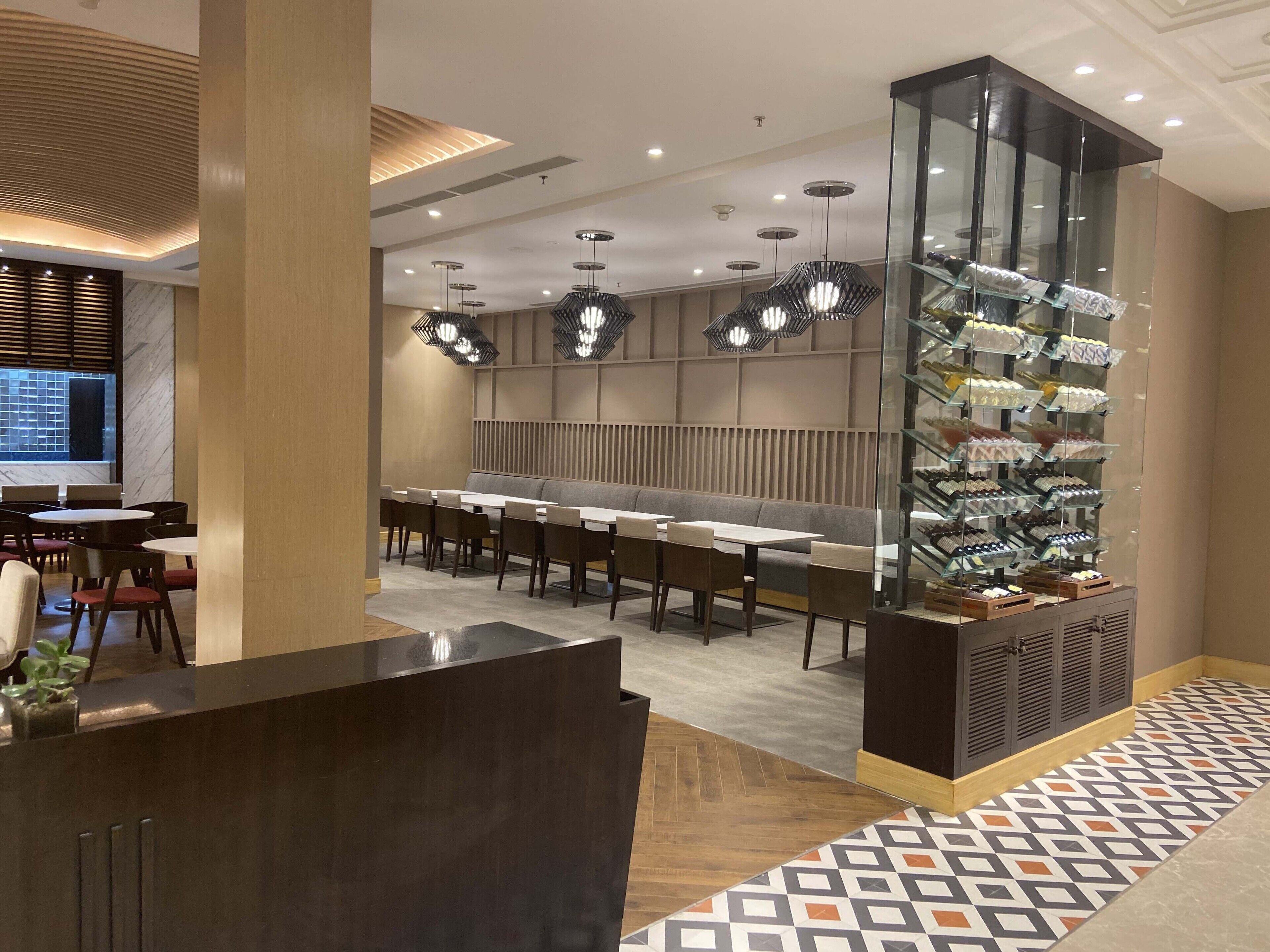 A modern restaurant interior with a long counter, multiple tables, and a glass display case with food items.