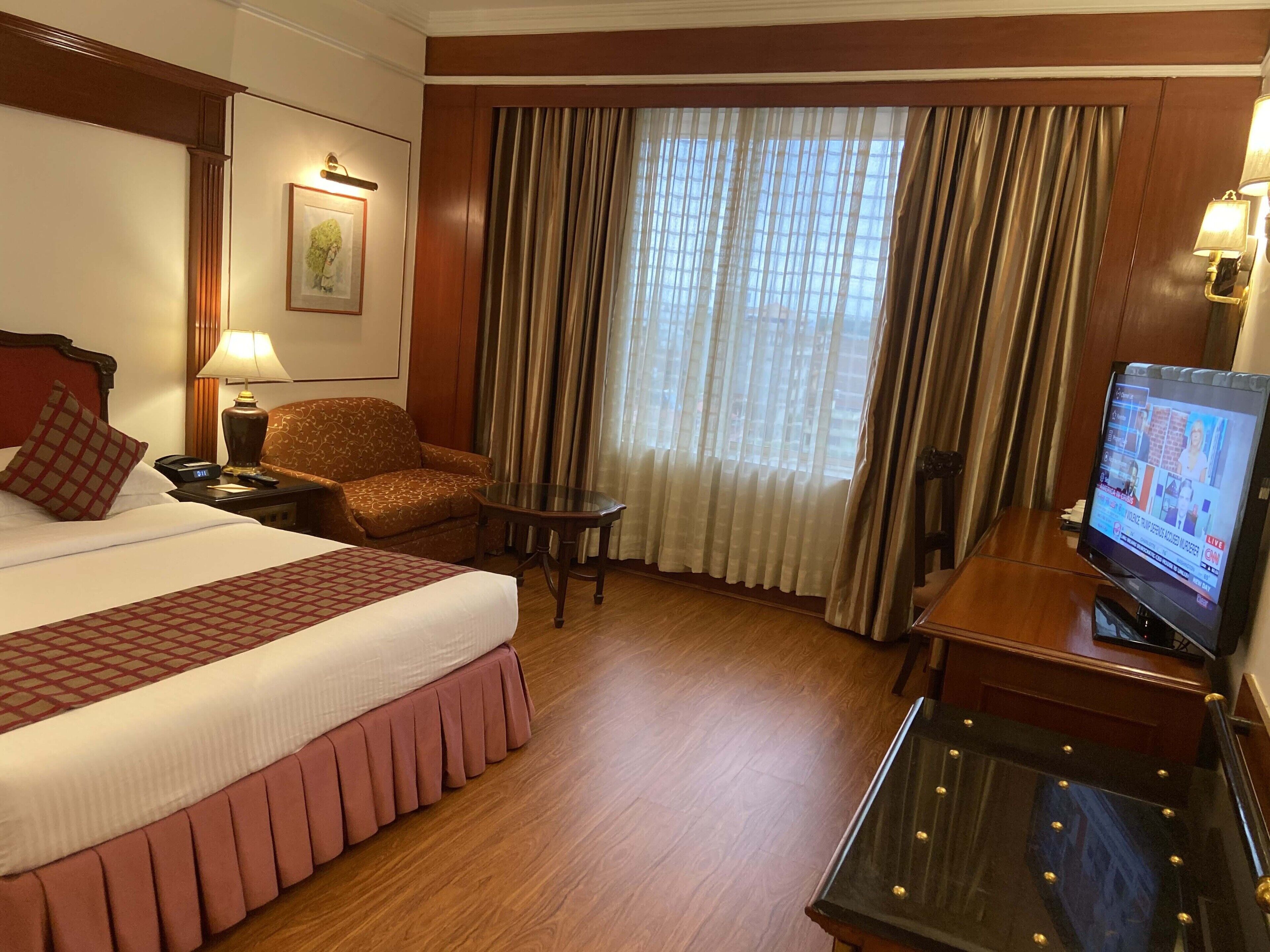 Ein Hotelzimmer mit einem großen Bett, einem Schreibtisch mit Fernseher, einem Sessel und einem kleinen Tisch.