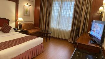 Ein Hotelzimmer mit einem großen Bett, einem Schreibtisch mit Fernseher, einem Sessel und einem kleinen Tisch.