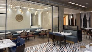 Un interior de restaurante moderno con techos altos, iluminación colgante y una variedad de opciones de asientos, incluyendo mesas y cabinas.