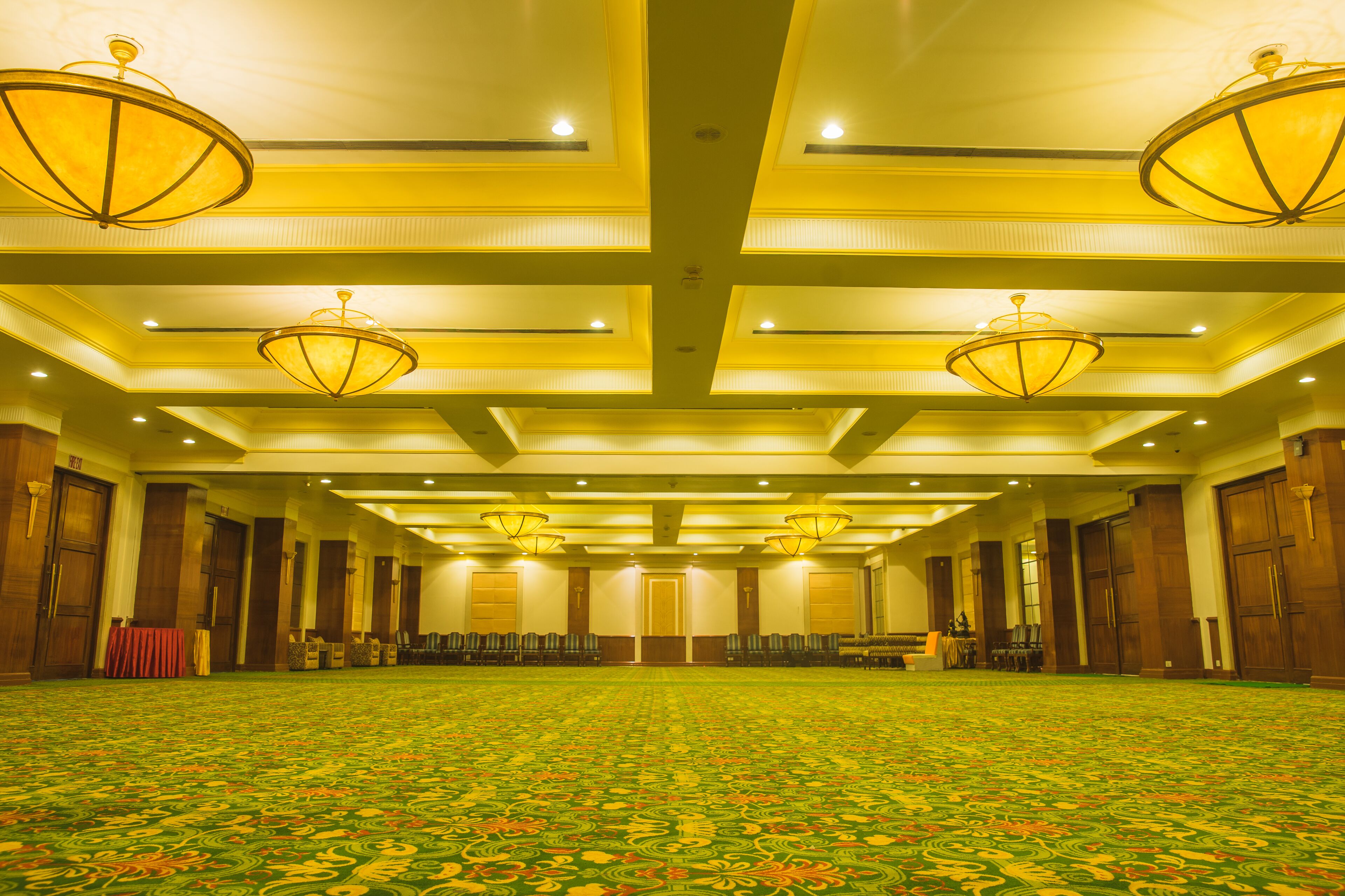 A spacious conference room with a patterned carpet, wooden paneling, and multiple chandeliers.