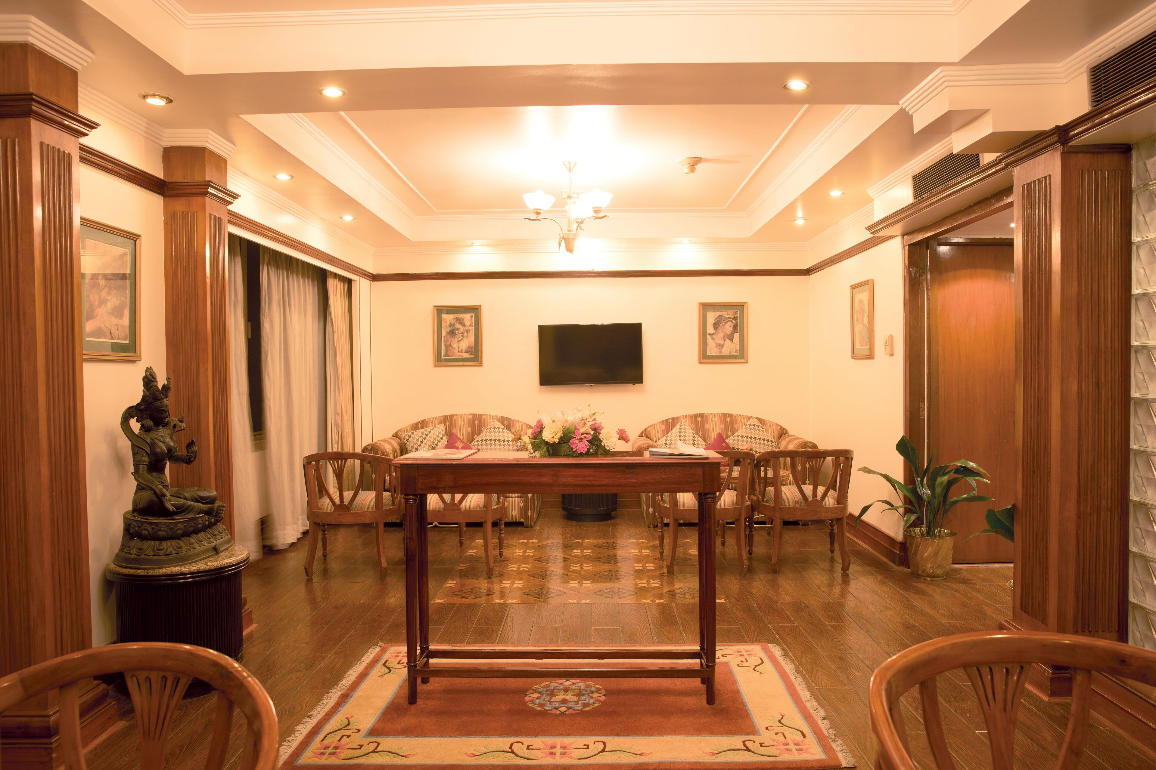 A formal room with a wooden table, chairs, a sofa, a television, and a statue.