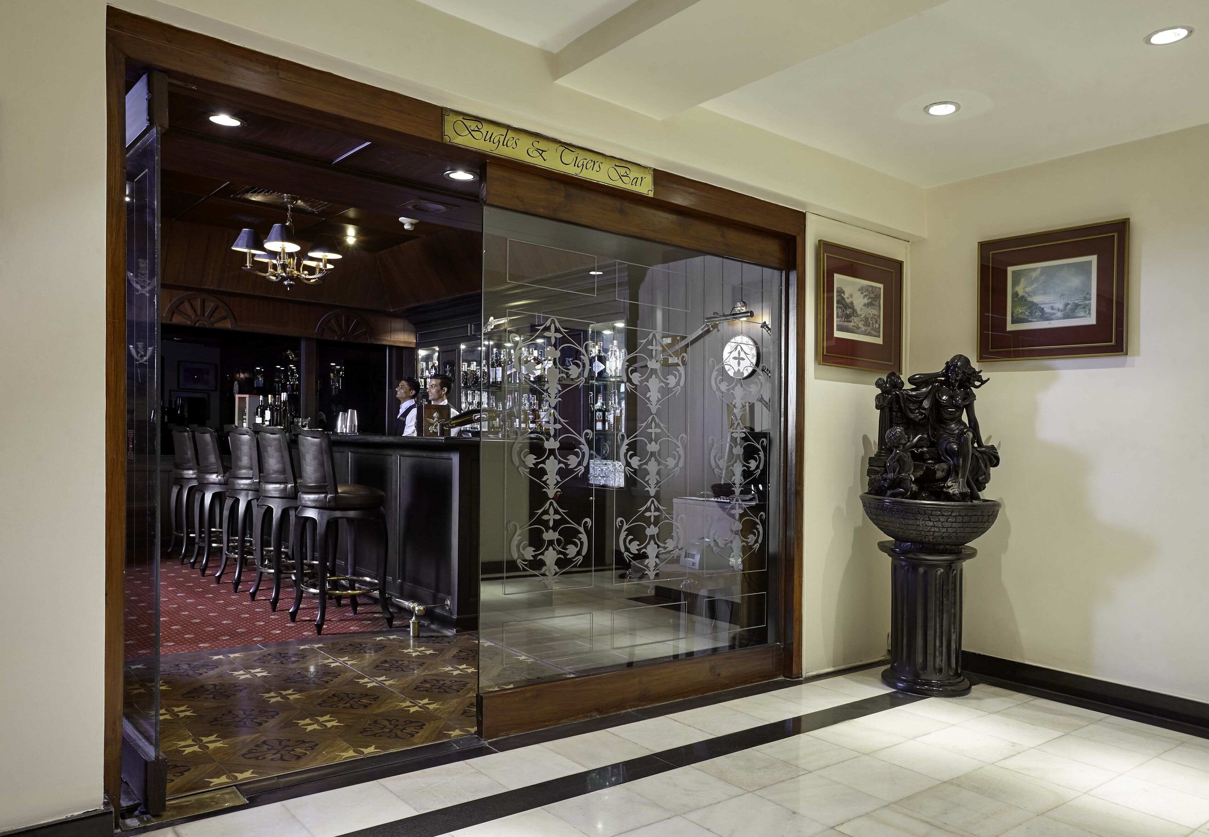 Uma área de bar com divisória de vidro, banquetas e um relógio decorativo.