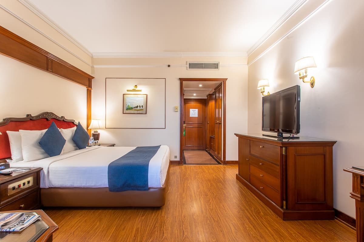 Een hotelkamer met een groot bed, een houten dressoir, een televisie en een ingelijste foto aan de muur.
