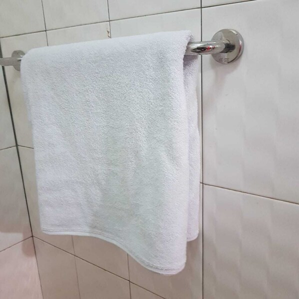 A white towel hanging on a metal towel rack attached to a tiled wall.