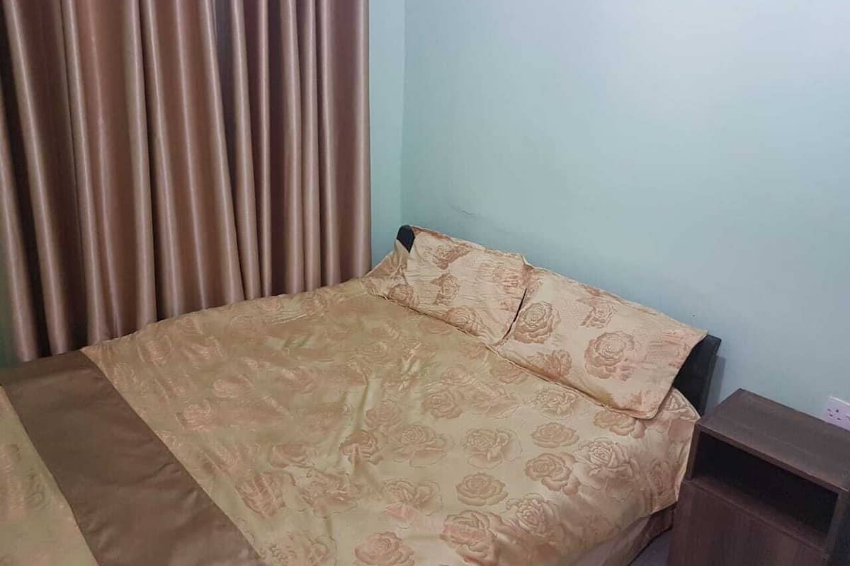 A bed with a floral bedspread and pillows, a wooden nightstand, and a curtain.