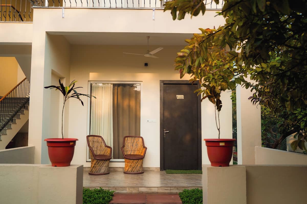 Une entrée moderne avec un escalier, deux fauteuils en osier, une plante en pot et une porte portant un numéro.