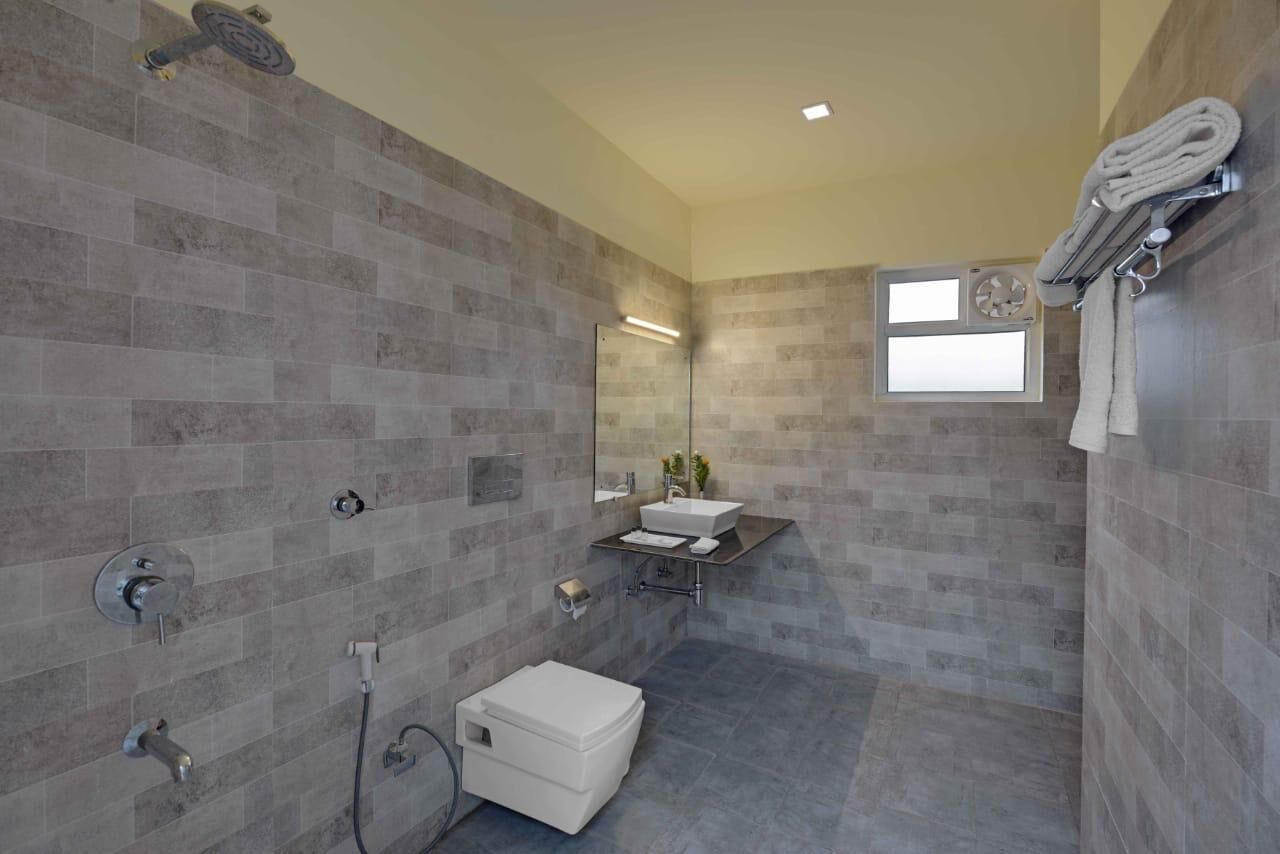 A modern bathroom with grey tiles, a white toilet, a sink with a mirror, and a towel rack.