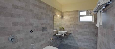 A modern bathroom with grey tiles, a white toilet, a sink with a mirror, and a towel rack.