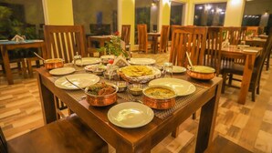 Uma sala de jantar com mesas e cadeiras de madeira, diversos pratos e vista para o exterior.