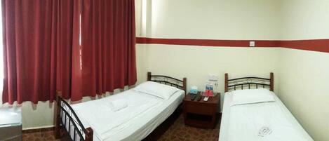 A room with two single beds, a nightstand with a lamp, a red curtain, and a tiled floor.