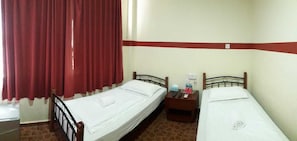 A room with two single beds, a nightstand with a lamp, a red curtain, and a tiled floor. - Warisan Family Inn (Semporna)