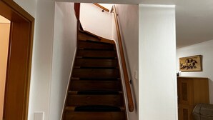 Una escala de fusta amb barana que condueix a un aterradora, on hi ha un interruptor de llum i un quadre penjat a la paret.