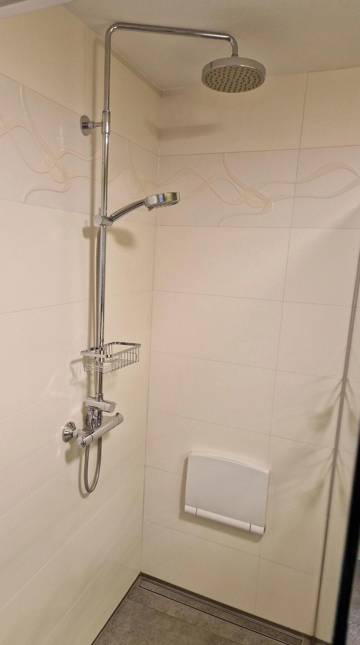 Een douche met een handdouche, een tweede handdouche en een douchekop aan de muur.