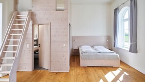 Un dormitorio con escaleras de madera, una cama y un ventanal con cortinas.