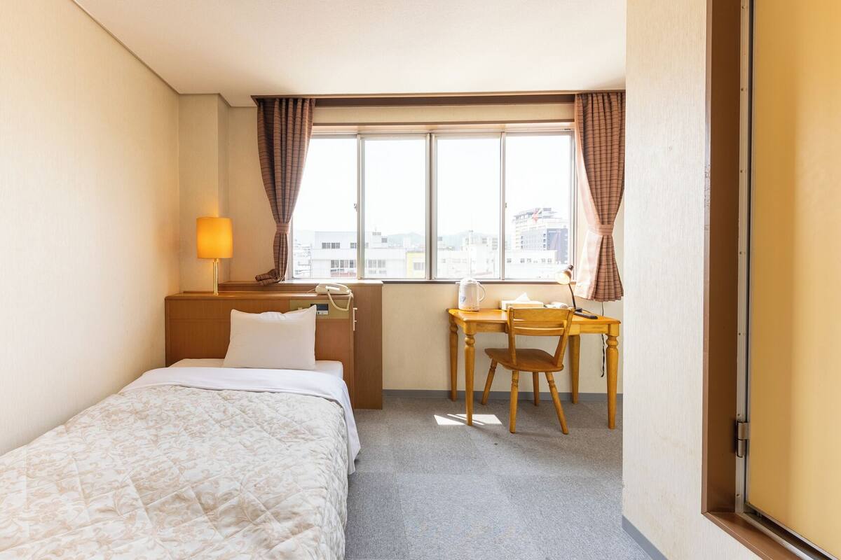 Una habitación de hotel con una cama, un escritorio, una silla, una lámpara y una ventana con cortinas.