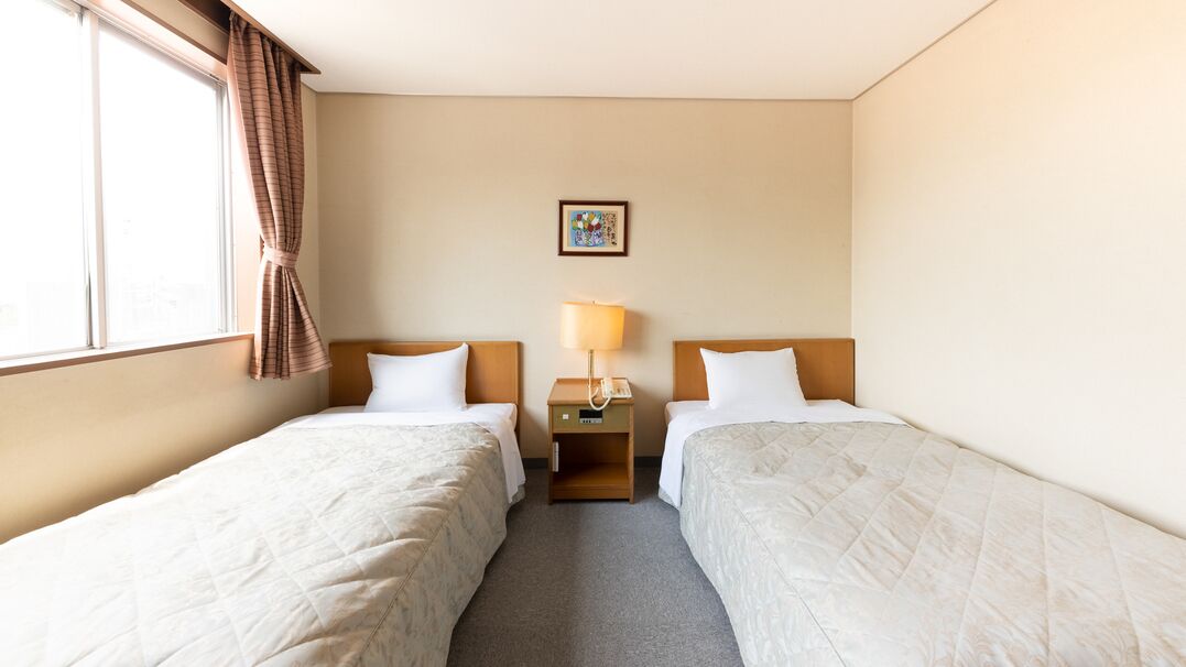 A hotel room with two beds, a nightstand with a lamp, a picture on the wall, and a window with curtains.