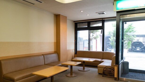 A seating area with a sofa and two tables, a door with a view of the street, and a trash can. - Tabist Kanko Business Hotel Matsuyama Hida Takayama (Takayama)