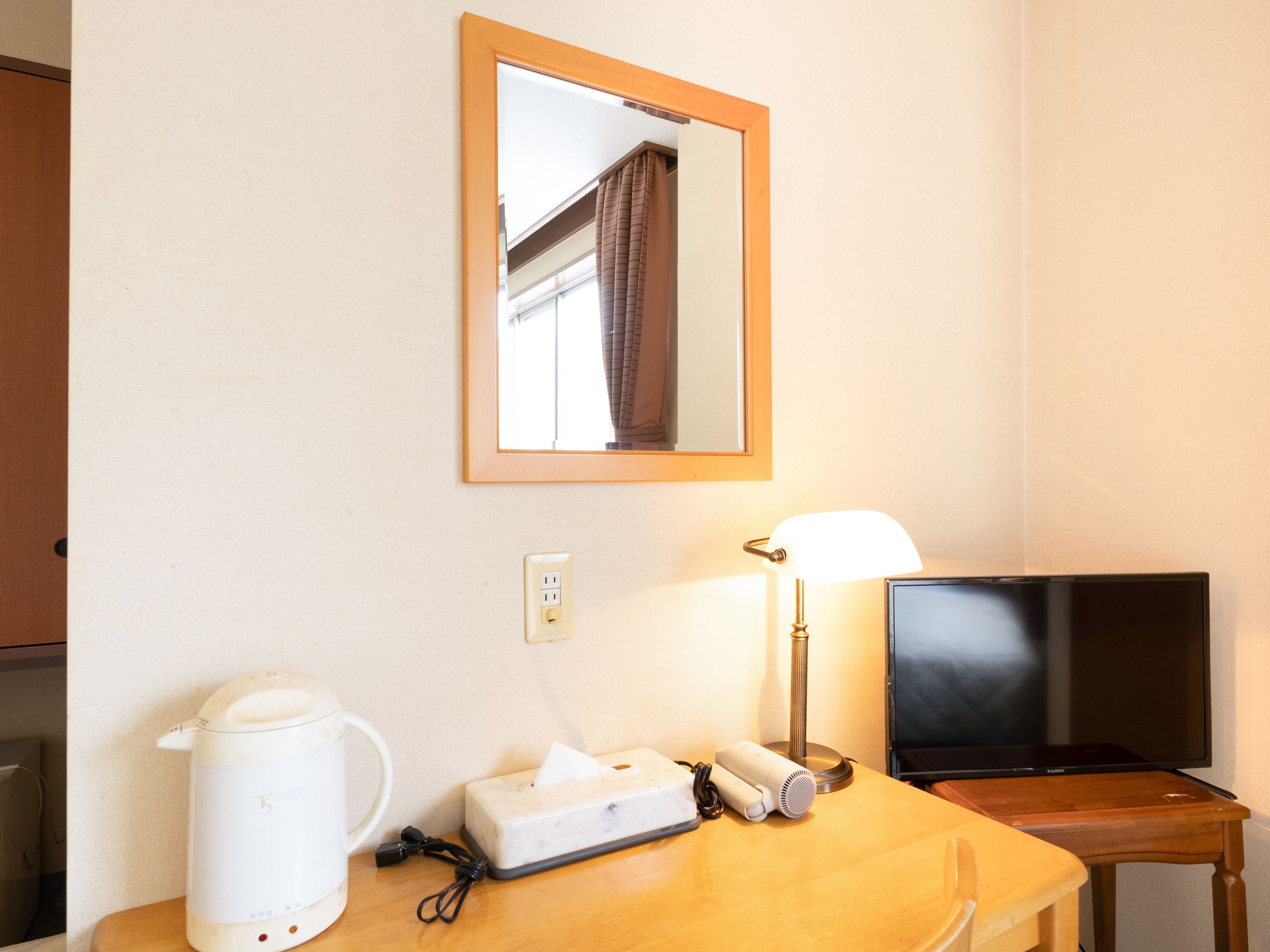 Ein Hotelzimmer mit einem Holztisch, einem weißen Wasserkocher, einer Taschentuchbox, einer Lampe und einem Fernseher.