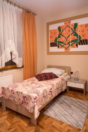 A bedroom with a bed, a nightstand, a lamp, a window with curtains, and a wall with artwork. - Rooms Vlado (Daruvar)