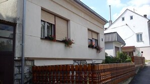 A building with a beige facade, two windows with shutters, and a decorative wooden fence. - Rooms Vlado (Daruvar)