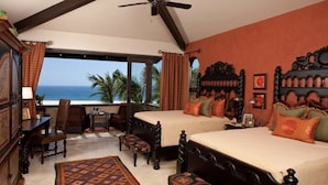 A bedroom with two beds, a desk, and a view of the ocean.