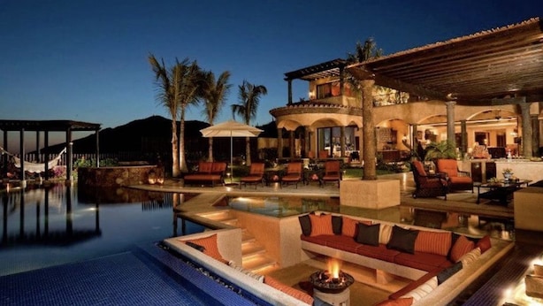 A luxurious pool area with a fire feature, outdoor seating, and a covered patio.