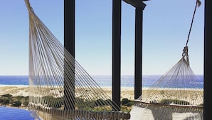 A hammock under a covered area with a view of the beach and ocean.