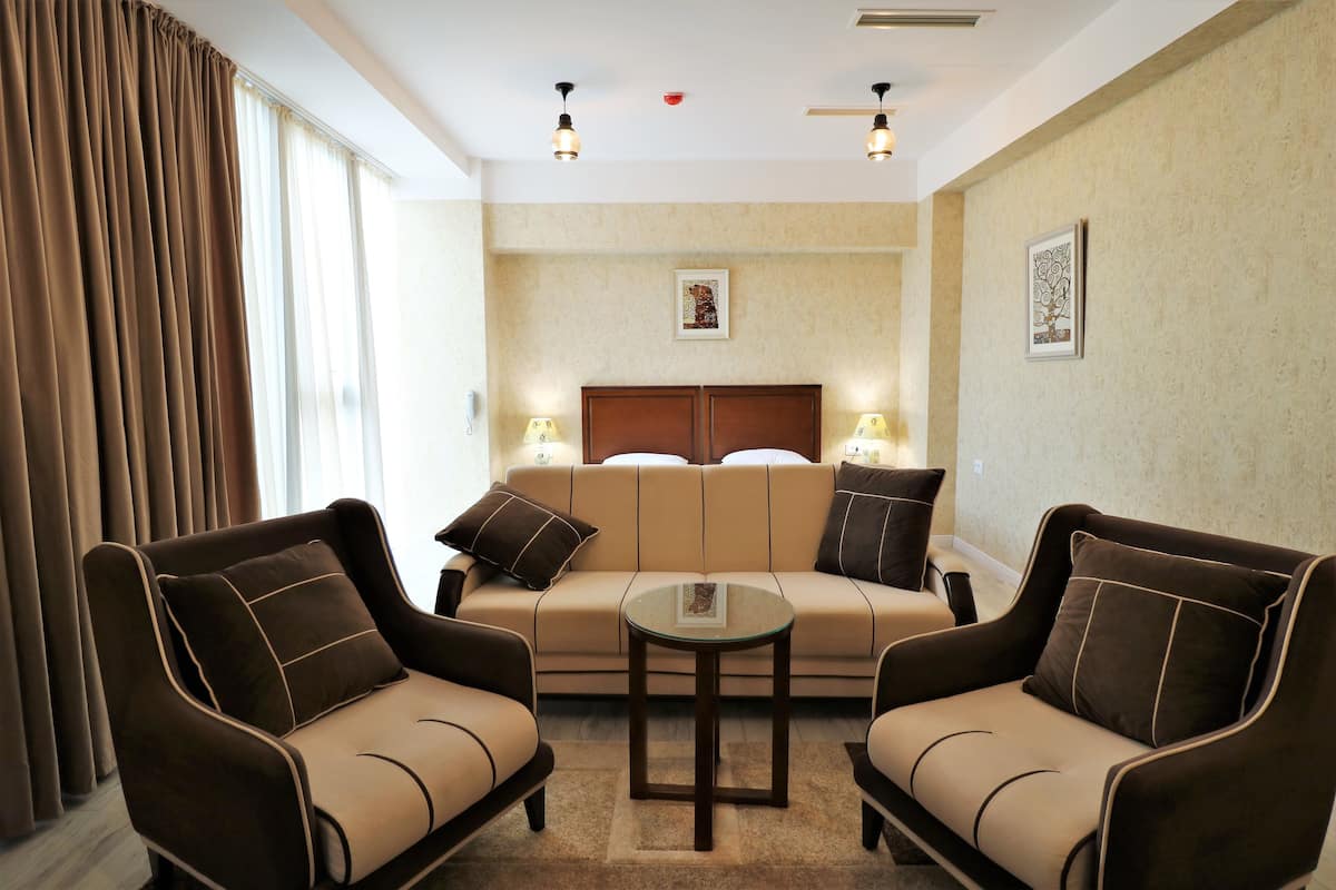 A modern hotel room with a sofa set, two armchairs, a small coffee table, and a large window with curtains.
