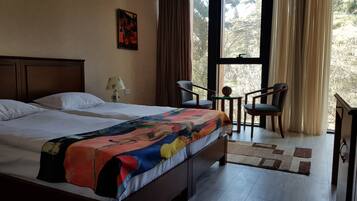 A hotel room with a large bed, two chairs, a small table, and a window with curtains.