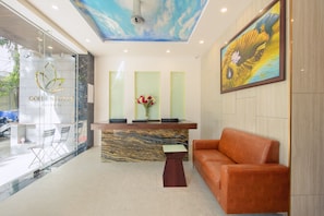 A reception area with a marble counter, a wooden side table, and an orange sofa. - Titan Hotel (Formerly known as Golden Lotus Central) (Nha Trang)