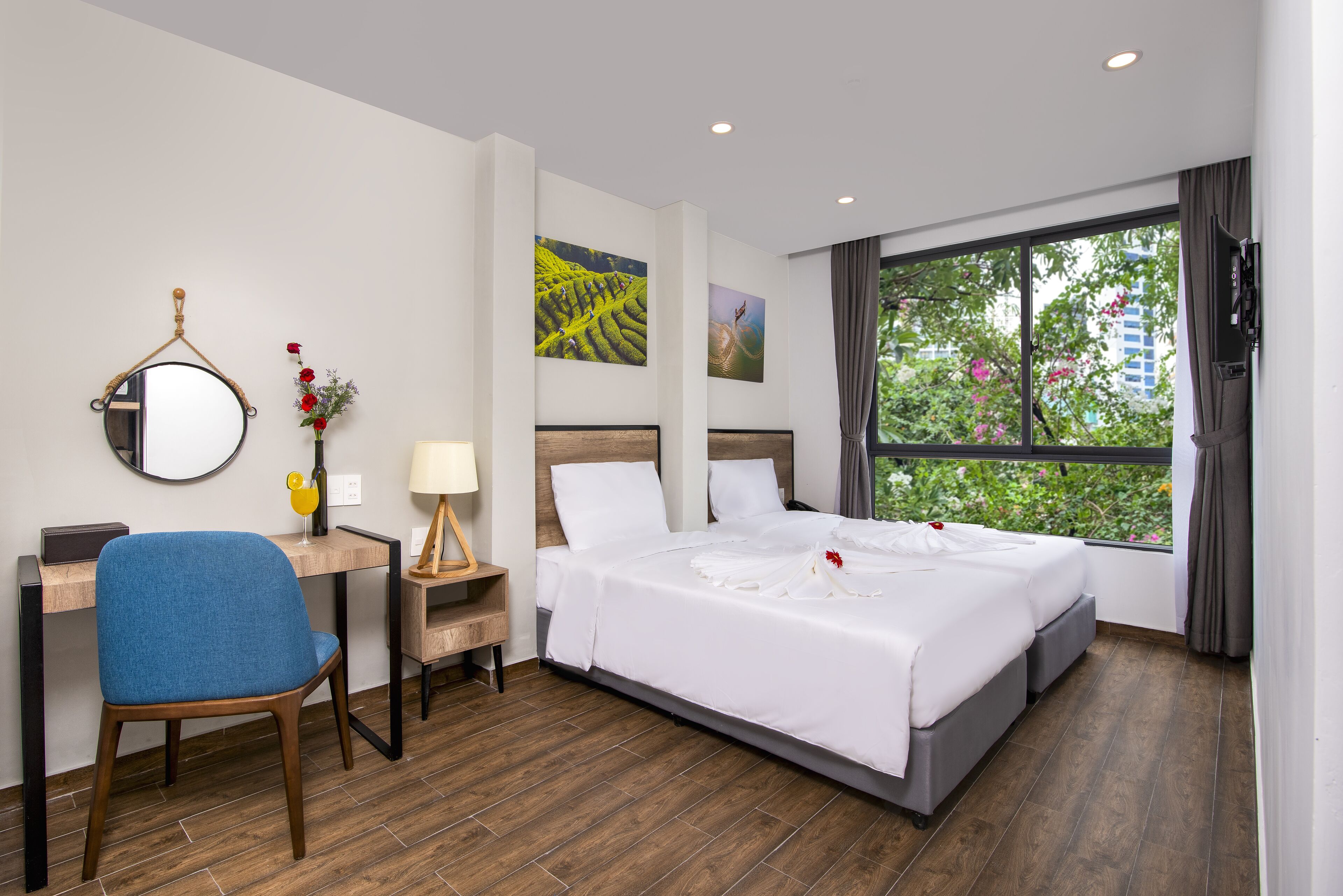A hotel room with a bed, a desk with a chair, a mirror, and artwork on the walls.