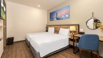 Ein Hotelzimmer mit einem großen Bett, einem Schreibtisch mit Stuhl, einem Nachttisch und einem Gemälde, das einen Sonnenuntergang über einer Brücke zeigt.