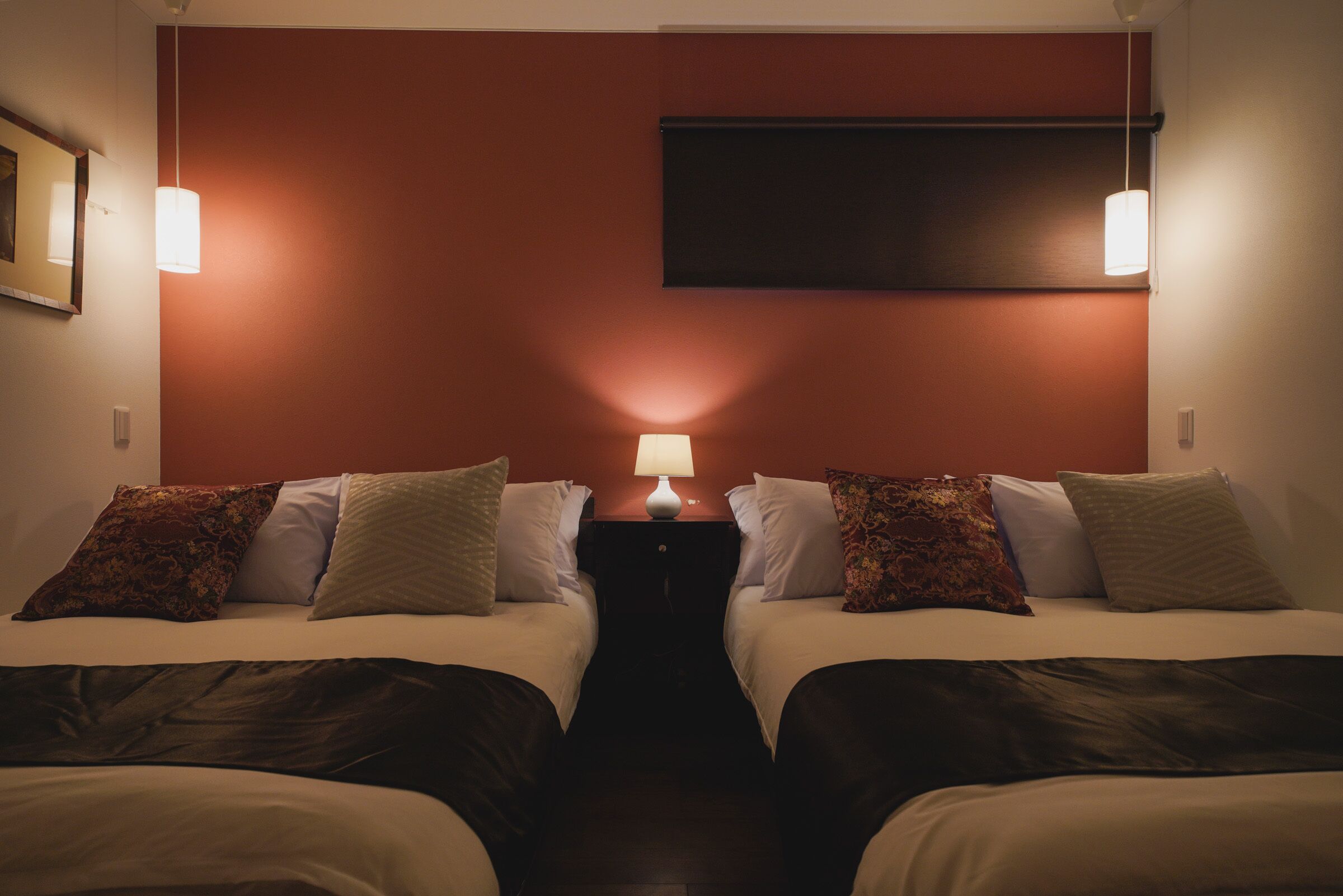 A hotel room with two beds, a nightstand with a lamp, and a TV mounted on the wall.