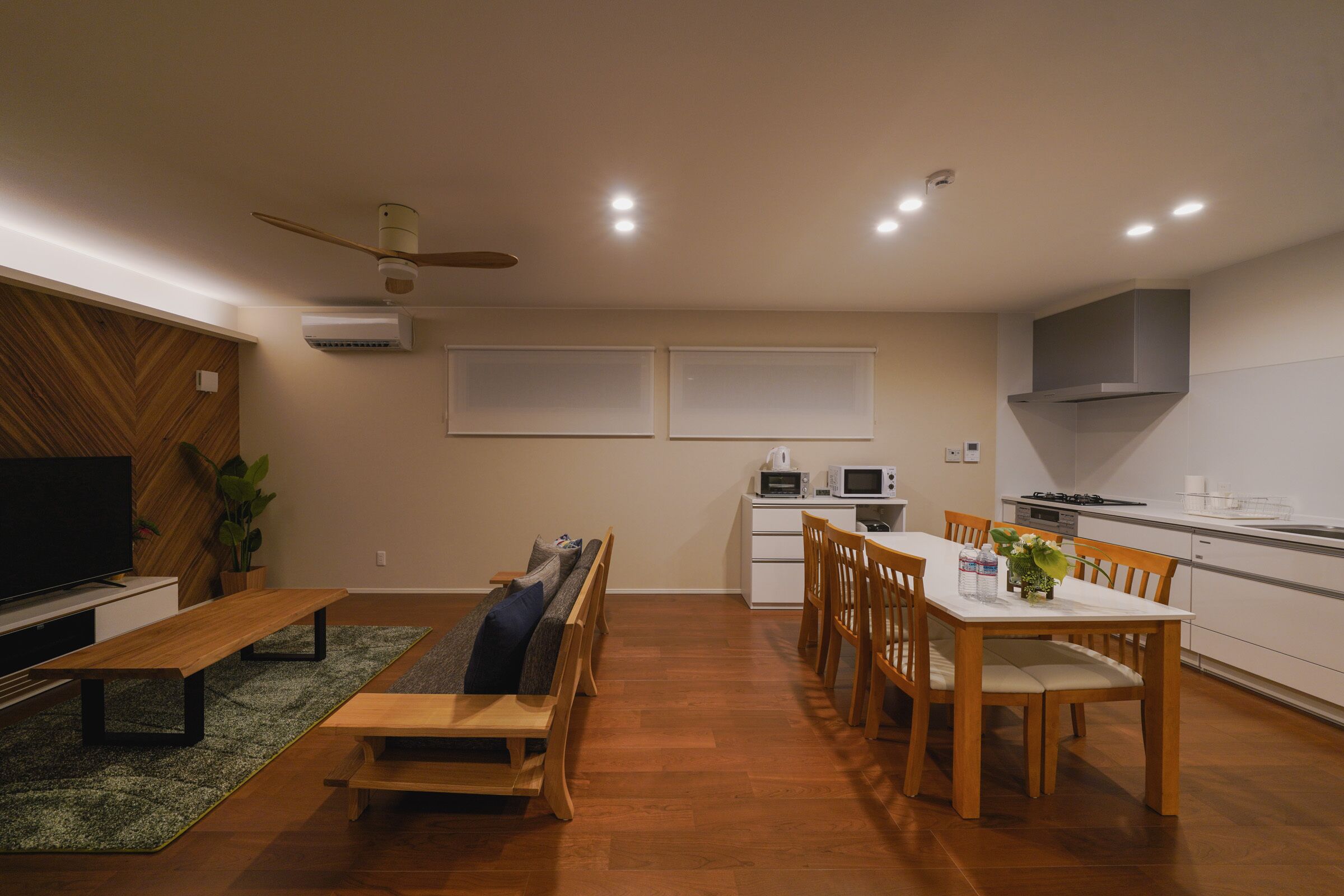 A modern kitchen with a dining area, built-in appliances, and a seating area with a TV and plant.