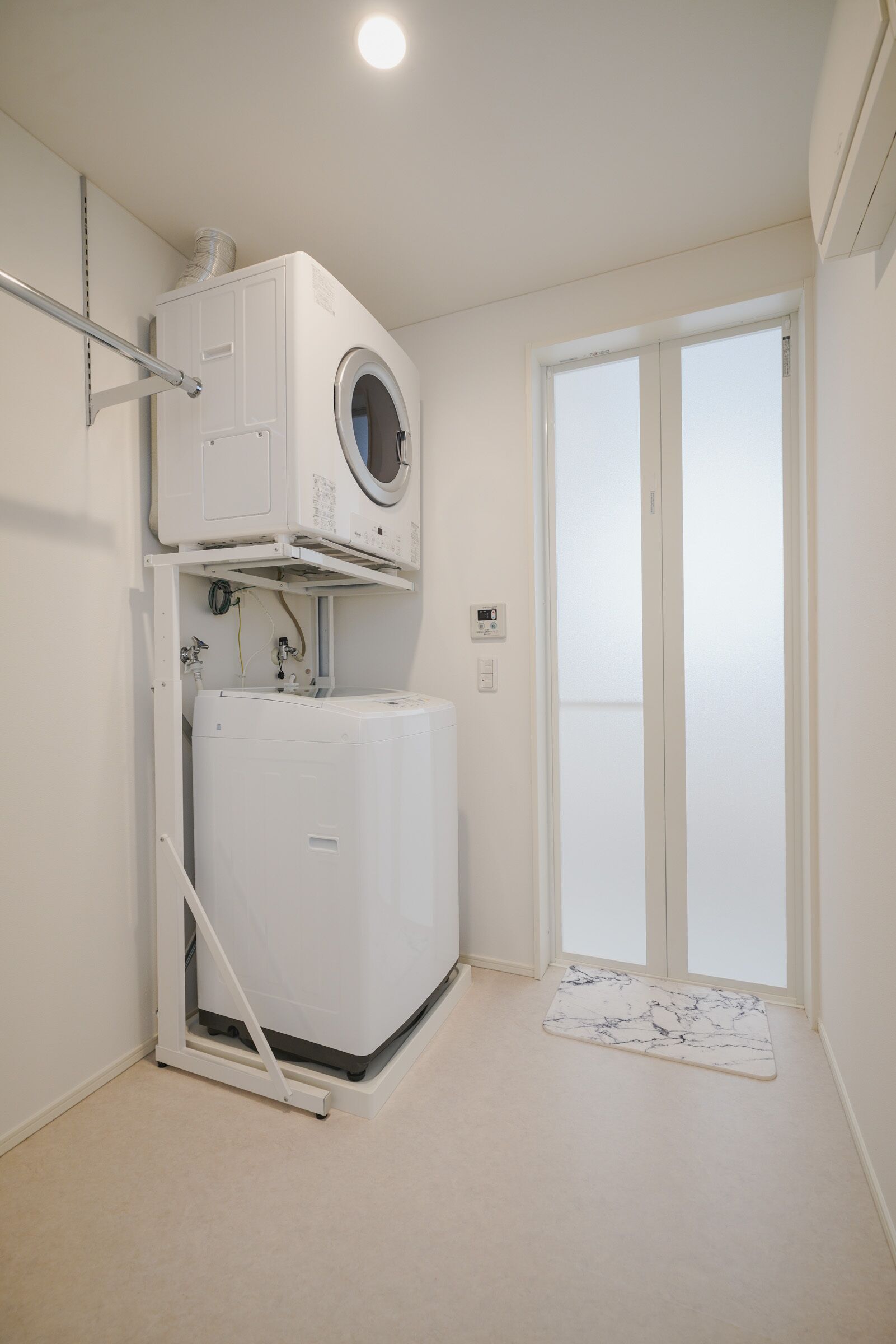 A laundry room with a washer and dryer, a door to a balcony, and a marble-patterned mat.