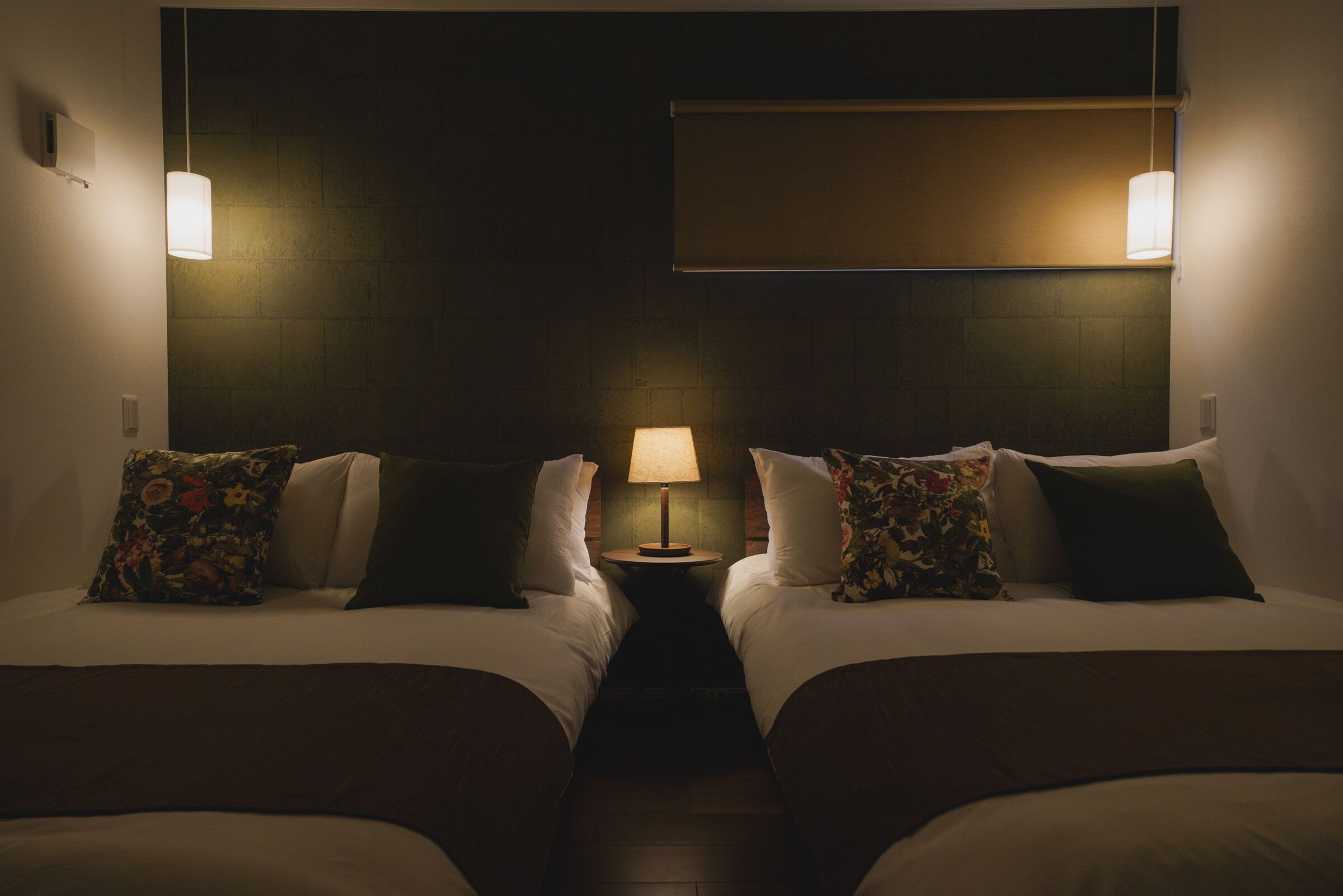 Une chambre d’hôtel avec deux lits, une table de chevet avec une lampe et un luminaire fixé au mur.