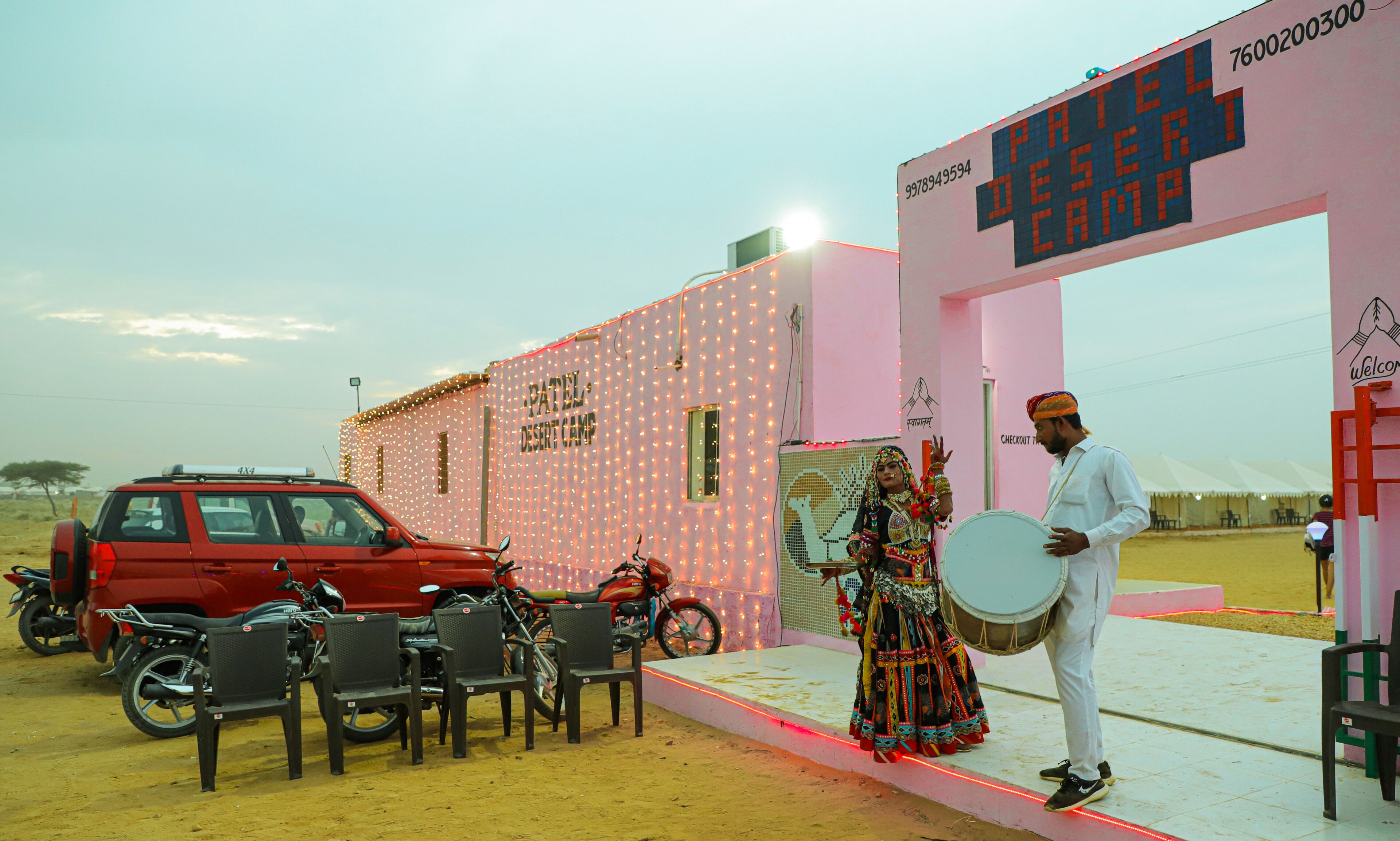 A stage with a sign reading "PATEL DESERT CAMP" and a person playing a drum.