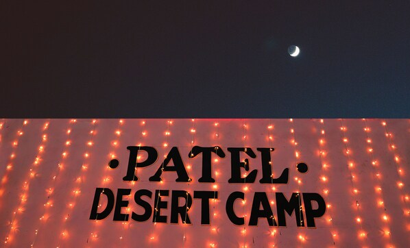 A sign with the text "PATEL DESERT CAMP" illuminated by string lights.