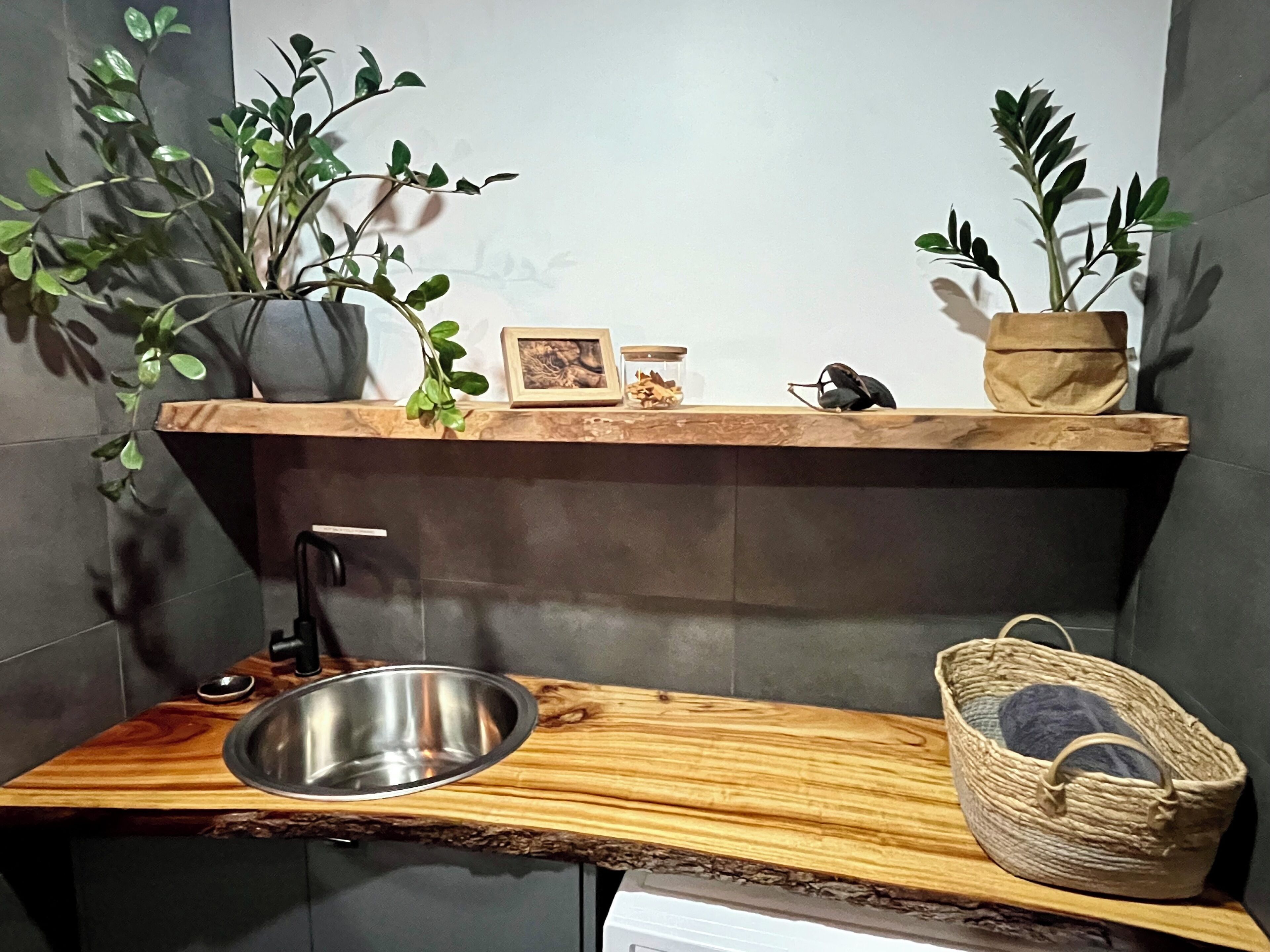 Eine Küche mit einer Holzausziehtafel, einem Edelstahlspülbecken, einer Topfpflanze, einem kleinen gerahmten Bild und einem gewebten Korb.