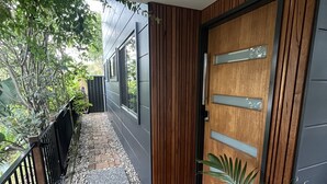 Un edificio moderno con una puerta de madera, un balcón con barandilla metálica y una planta en maceta.
