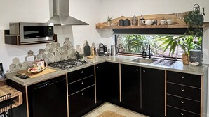 Una cocina moderna con gabinetes negros, una campana extractora de acero inoxidable, un microondas y un horno empotrado. Hay una ventana con vistas a zonas verdes.