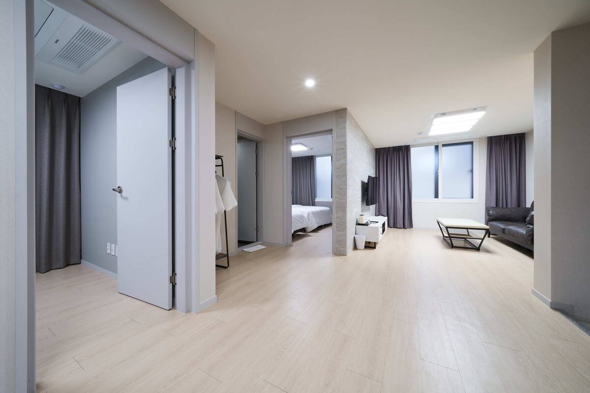 A modern hotel room with a wooden floor, a bed, a desk, a chair, and a sofa.